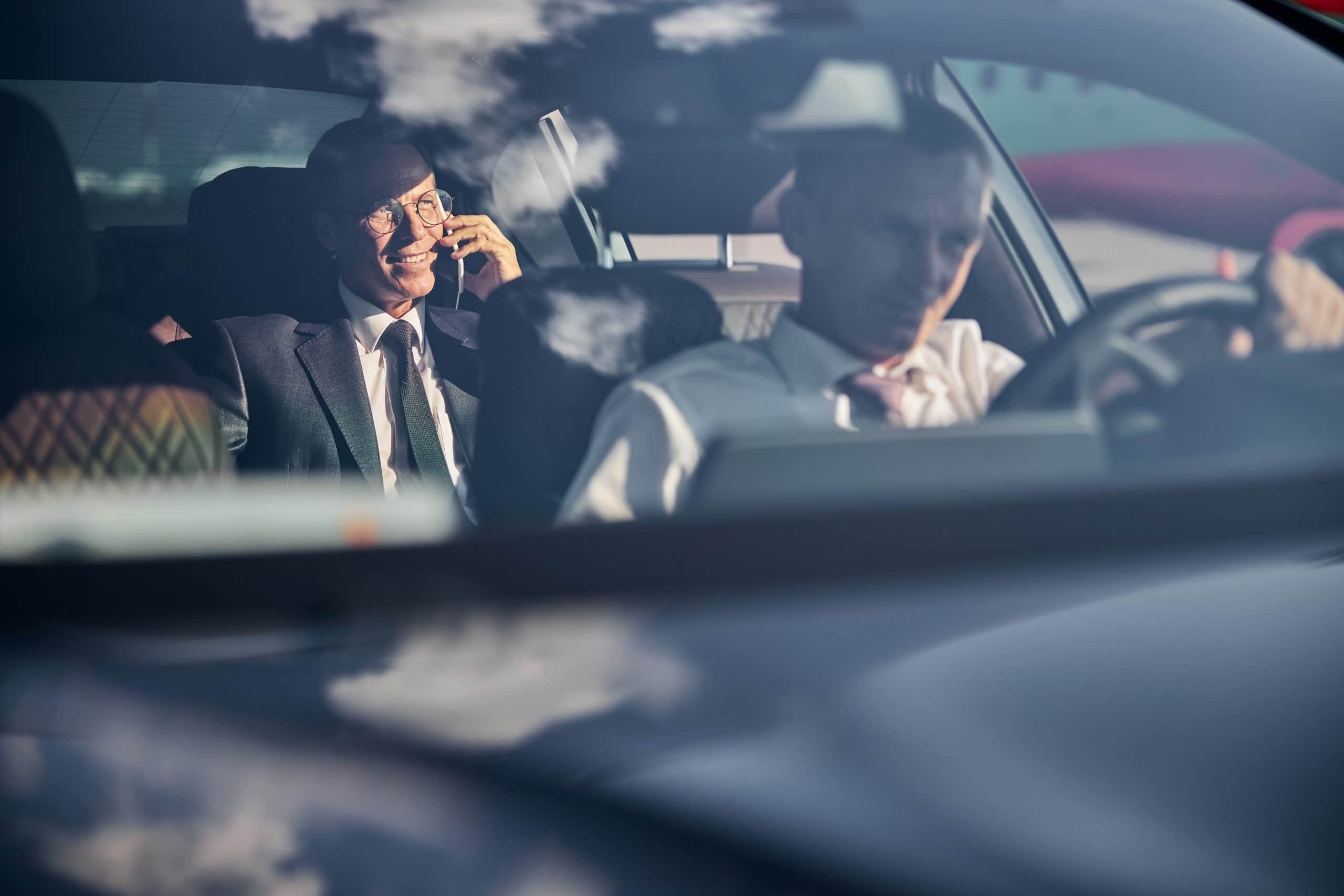 Smiling businessman with smartphone travelling with chauffeur